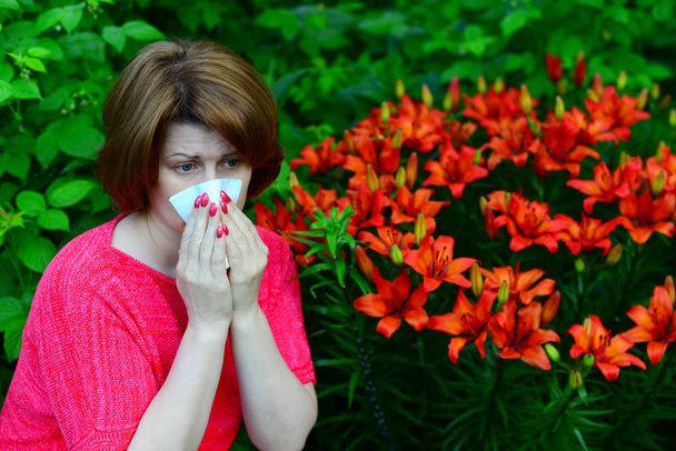 woman with an allergic rhinitis near lilies in nature - Foto, afbeelding