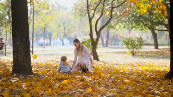 Zeitlupenaufnahmen von fröhlichen Babys, die mit der Mutter Blätter im Herbstpark werfen - Filmmaterial, Video