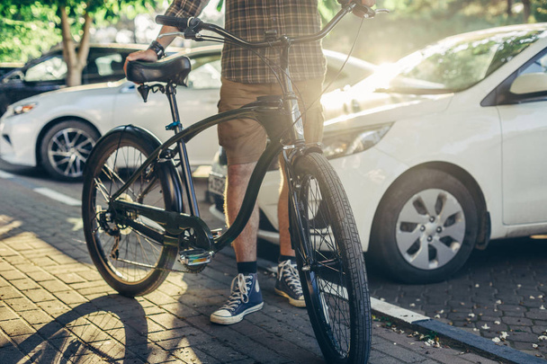 Hombre adulto irreconocible de pie con bicicleta cerca de los coches de verano estilo de vida rutinario diario
 - Foto, imagen