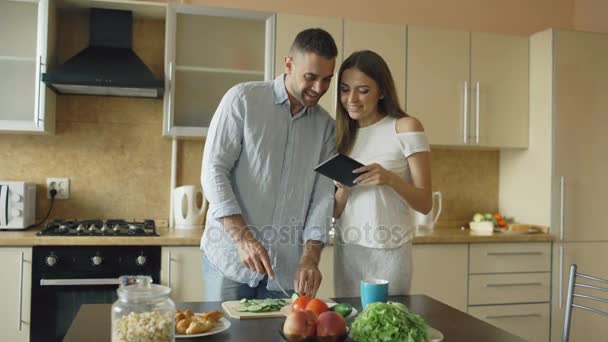 Attractive couple meet in the kitchen early morning. Handsome woman using tablet sharing his husband social media - Imágenes, Vídeo