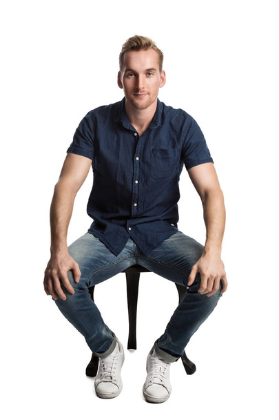 Man in blue shirt and jeans sitting down - Zdjęcie, obraz