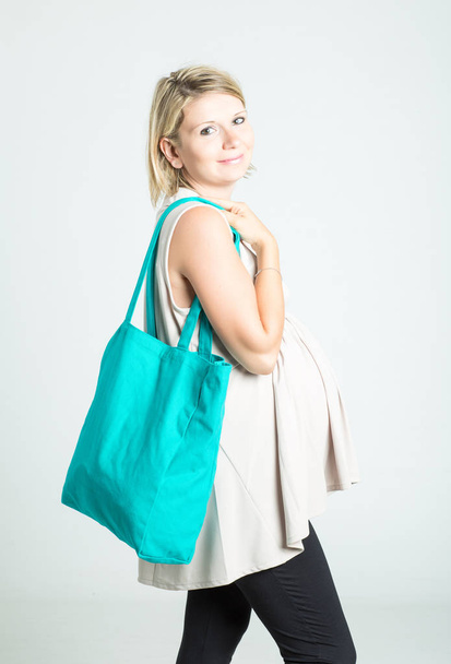 Beautiful young blonde pregnant woman with shopping bags posing. Pregnancy, motherhood, sale, people and expectation concept. Isolated on background. - Фото, зображення
