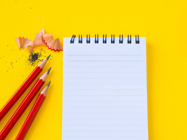 Sharpening a red pencil sharpener and the note book On yellow background. - 写真・画像