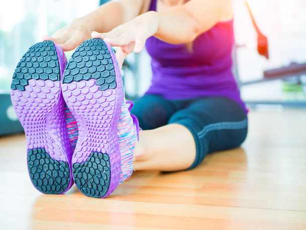 Mujer en forma estirando su pierna para calentarse en la sala de gimnasio con equipos de fitness en el fondo
 - Foto, imagen