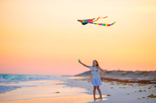 Little girl with flying kite on tropical beach at sunset. Kid play on ocean shore. Child with beach toys. - Photo, Image