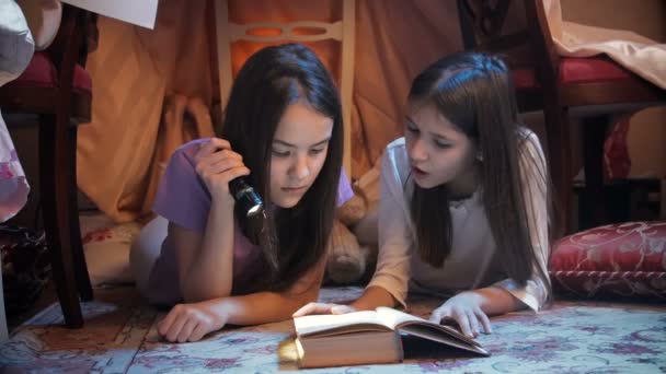 4k Video von zwei Mädchen, die Buch mit Taschenlampe im Tipi-Zelt lesen - Filmmaterial, Video