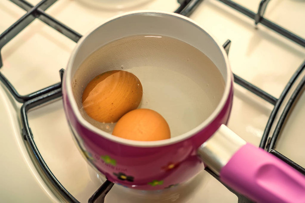 Fervendo dois ovos em água na panela de aço inoxidável
 - Foto, Imagem