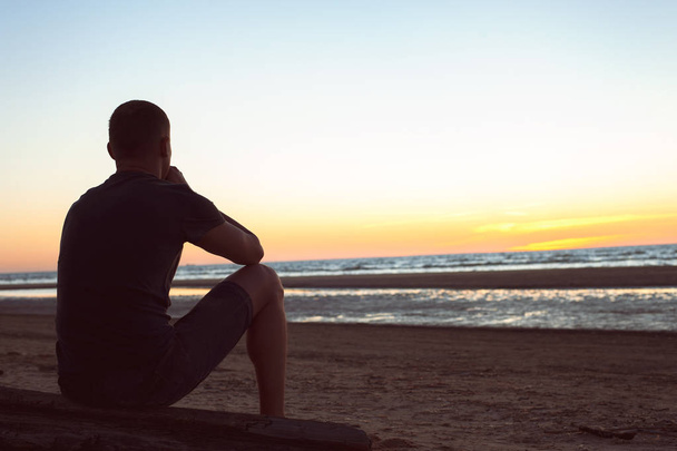 Burdened by unseen worries. Sad lonely man sits on beach - 写真・画像