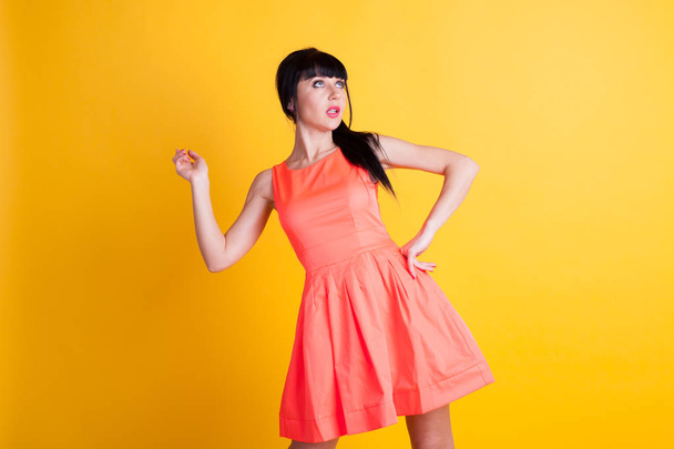 girl in orange dress on a yellow background hands up - Photo, Image