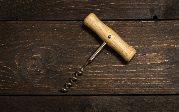 Corkscrew opener for wine cork on dark chocolate wooden background. Bottle-screw to open wine alcohol bottle at rustic vintage brown table. - Photo, Image