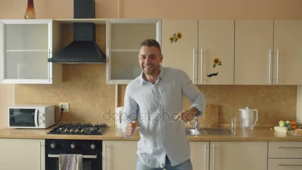Handsome young funny man dancing in kitchen at home in the morning and have fun on holidays - Séquence, vidéo