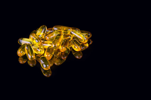 Cápsulas com óleo de peixe sobre fundo preto com reflexão, copyspace
 - Foto, Imagem
