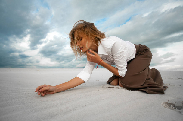 junge traurige Frau kniet in der Wüste auf Himmelshintergrund. - Foto, Bild