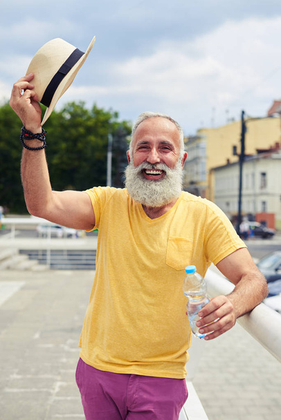 Smiley bearded man taking off hat while standing with bottle of  - Foto, Imagem