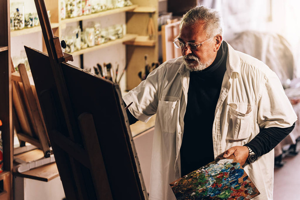 Old man artist painting oils in his studio. - Fotó, kép
