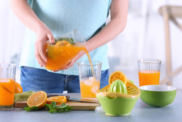 Woman pouring orange lemonade into glass in kitchen - Fotografie, Obrázek
