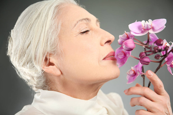 Beautiful elderly woman with orchid flowers  - Valokuva, kuva