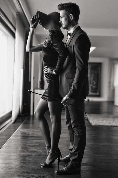 Young dominant rich man with whip embracing lover black and whit - Photo, Image