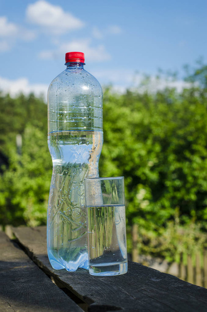 Trinkwasser in einem Glas aus einer Flasche auf einem Naturhintergrund - Foto, Bild