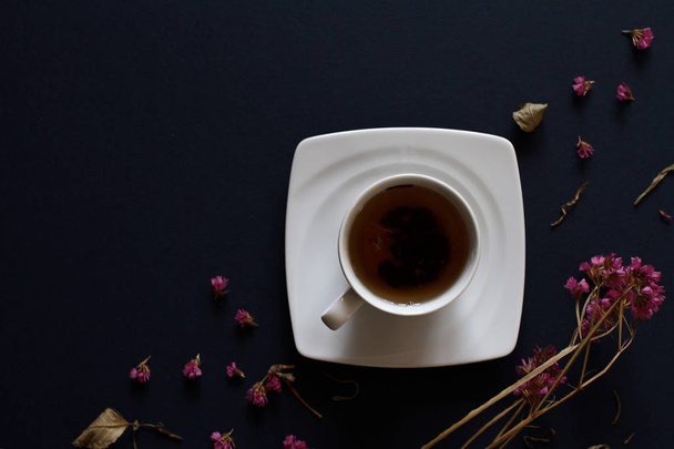Closeup of cup of tea on dark blue background with flowers. - Фото, изображение
