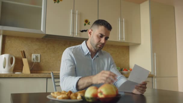 Uspet young man reading unpaid bills and hugged by his wife supporting him in the kitchen at home - Felvétel, videó