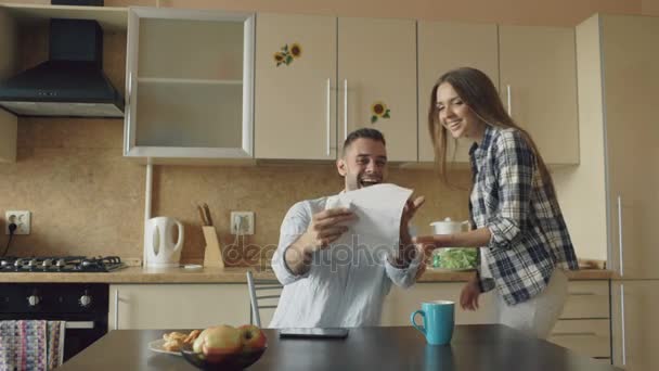 Attractive happy couple recieve good news unfolding letter in the kitchen while have breakfast at home - Filmmaterial, Video