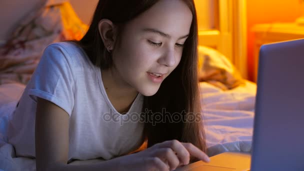 ベッドの上に横たわるとラップトップでビデオのメッセンジャー経由で話している 10 代の少女のクローズ アップ映像 - 映像、動画