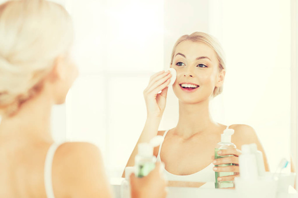 young woman with lotion washing face at bathroom - Foto, imagen