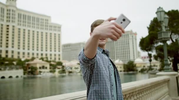 Young man is taking a selfie with the Bellagio hotel on the background - Кадри, відео