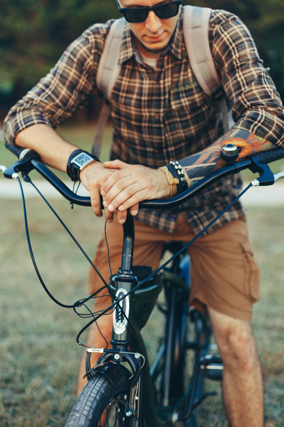Young Man Cyclist In Sunglasses With Bicycle In Summer Park During Sunset Vacation Traveling Relaxation Resting Concept - Photo, image