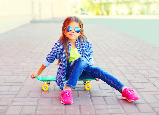 Fashion portrait little girl child sitting on skateboard in the  - Photo, Image