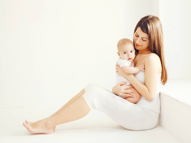 Happy young mother with baby at home in white room near window - Foto, imagen