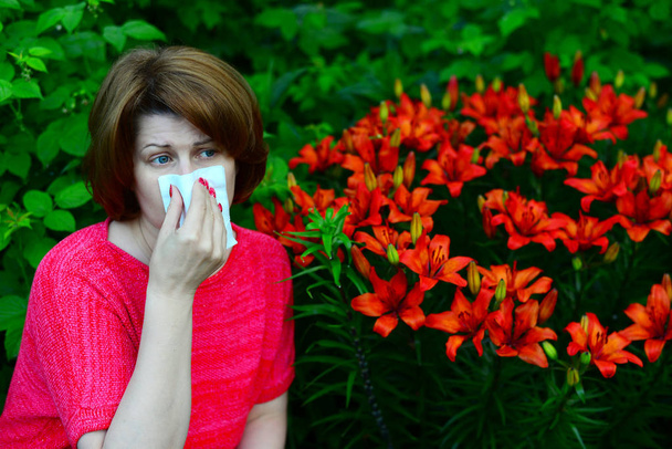 woman with an allergic rhinitis near lilies in nature - Foto, afbeelding