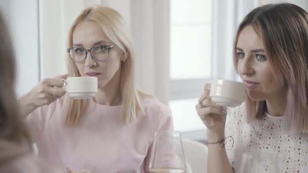 Two girls in restaurant drink tea and look at interlocutors opposite. - Video
