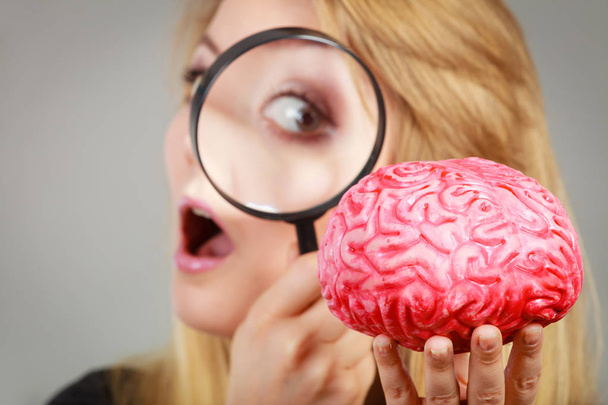 Woman holding magnifying glass investigating brain - Zdjęcie, obraz