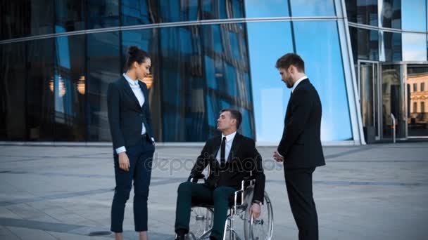 Behinderter Geschäftsmann im Rollstuhl und zwei seiner Kollegen unterhalten sich positiv - Filmmaterial, Video