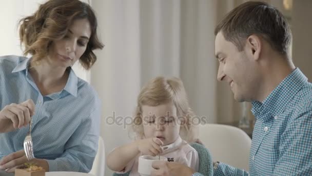 Parents with the child eat desserts and drink tea, adults help child - Imágenes, Vídeo