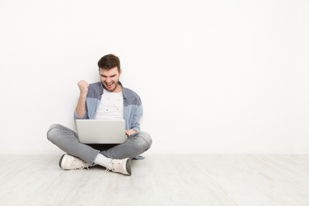 Young man playing on laptop sitting on floor - Фото, зображення