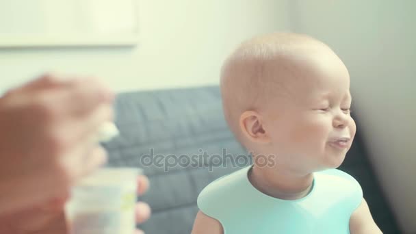 Iloinen pikkupoika aamiaisella. Tarkkaavainen rakastava äiti ruokkii vauvaa lusikalla. Hidastus
 - Materiaali, video