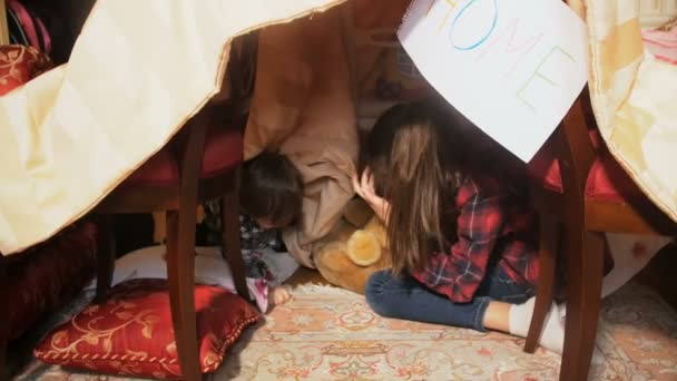 Oudere zus speelt met haar kleine broertje in eigen huis gemaakt van dekens - Video