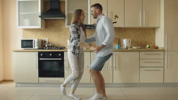 Attractive young joyful couple have fun dancing while cooking in the kitchen at home - Video, Çekim