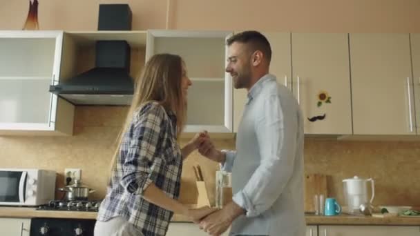 Attractive young joyful couple have fun dancing while cooking in the kitchen at home - Felvétel, videó