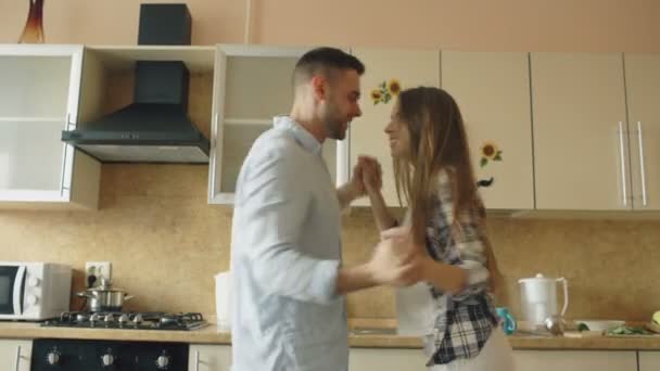Attractive young funny couple have fun dancing while cooking in the kitchen at home - Záběry, video