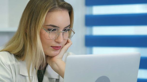 Young female nurse in glasses using laptop at desk in medical office - Foto, imagen