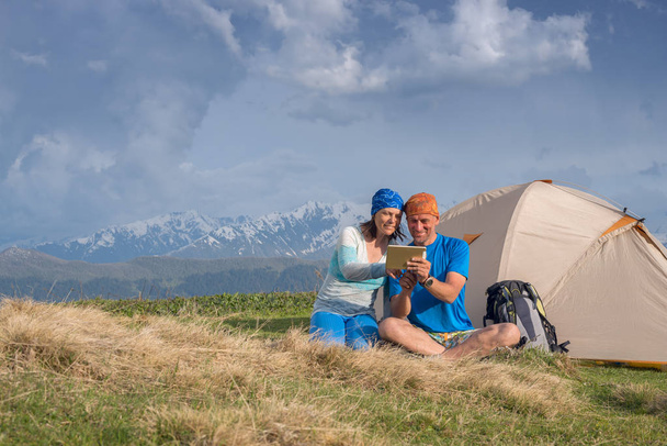 Joyful travelers sit next to tent use tablet and having fun - Photo, image