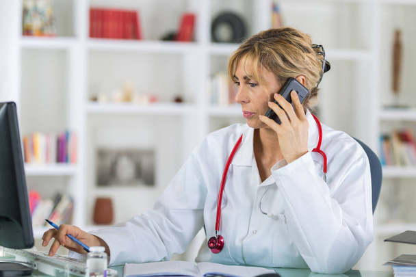 female doctor at her desk talking on phone - Фото, изображение