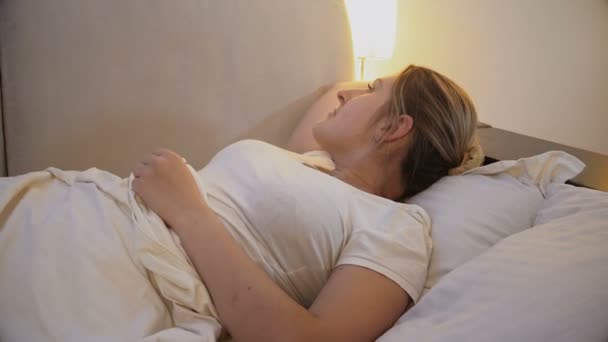 Young woman trying to fall asleep turning off bedside lamp - Footage, Video