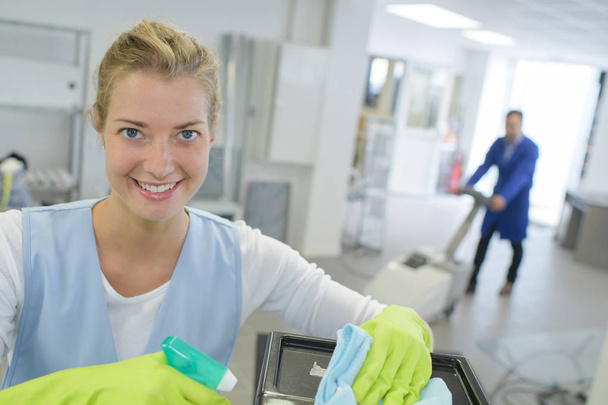 young female cleaner in apron with supplies working indoors - Foto, Bild