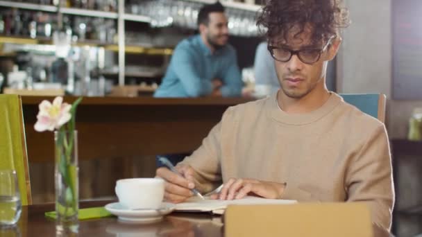 ヒスパニック系人種若い男居心地の良いコーヒー ショップでのノートブック タブレット コンピューターと作るノートを使用して. - 映像、動画