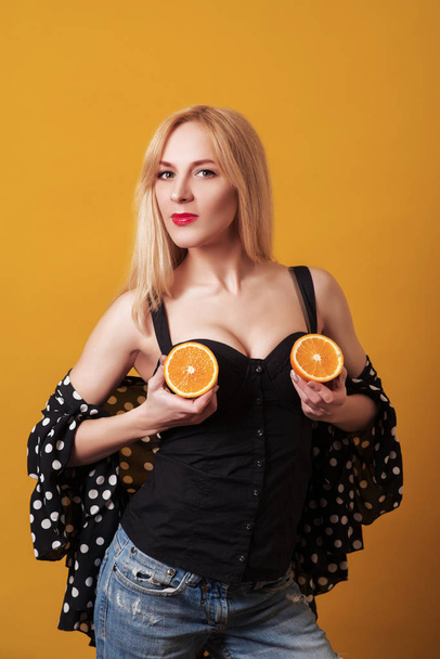 Happy young woman holding halvesof oranges isolated over yellow background. - Photo, Image